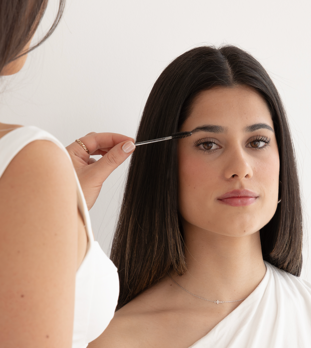 Woman getting her eyebrows done by another person with a white background